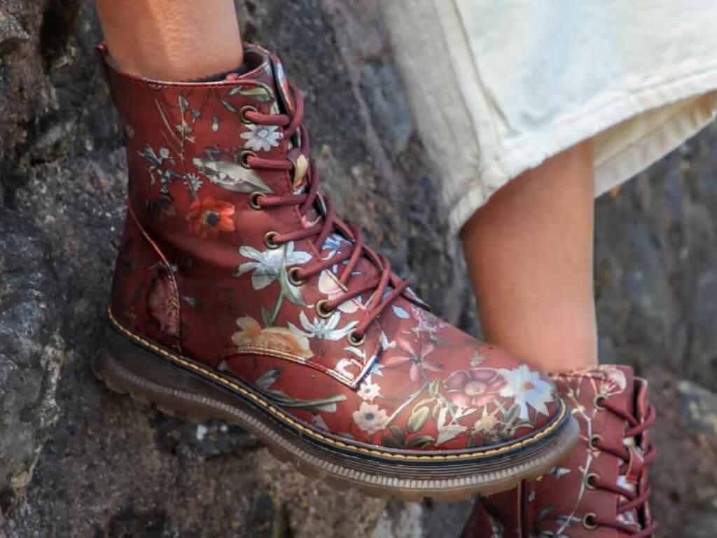 Photo of ankles and feet, person wearing pair of lace-up, high-top boots, burgundy with floral pattern