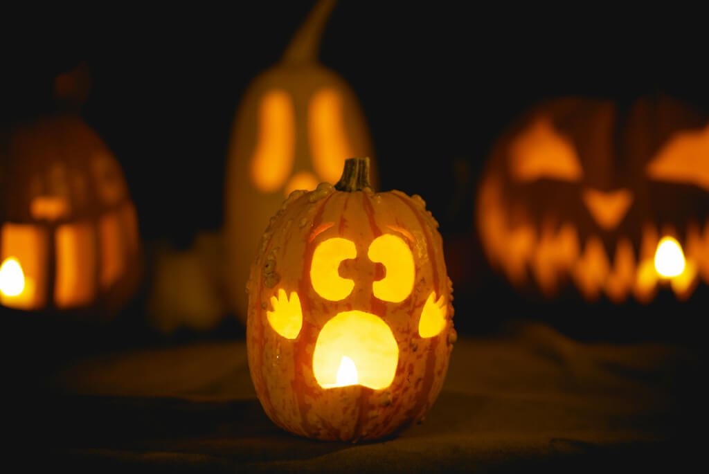 Night time line up of pumpkins carved with scary faces and candles
