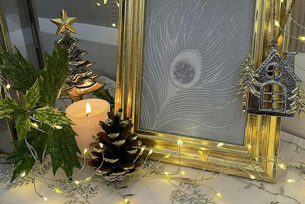 Gilded gold picture frame and two Christmas ornaments, decorated with a lit candle and warm fairy lights