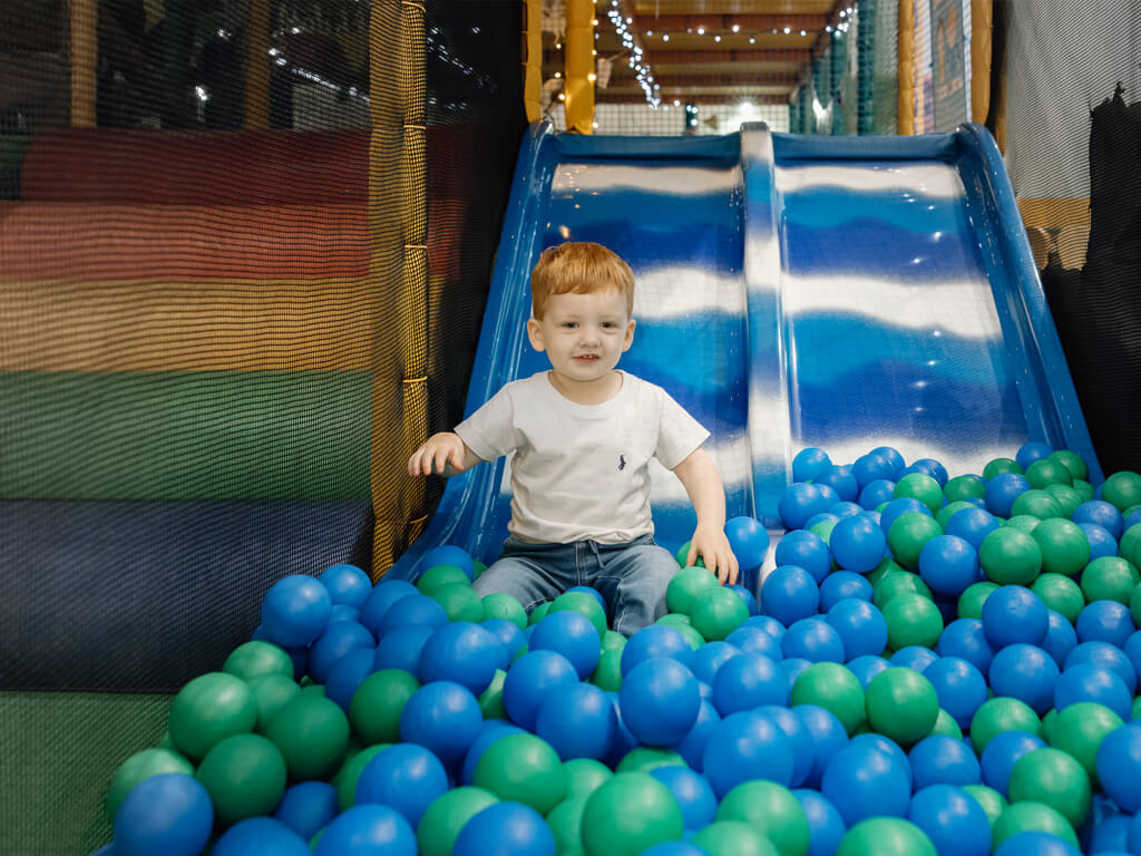 Child on a slide surrounded by blue and green plastic balls.
