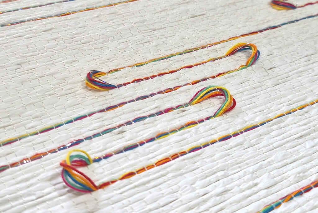 Handcrafted textile cream background and muti-coloured looping thread pattern