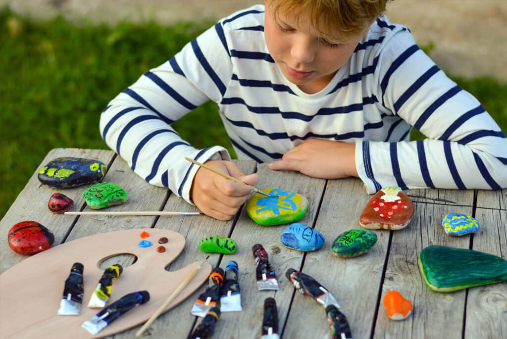 Young boy sat at a table decorating pebbles with paints