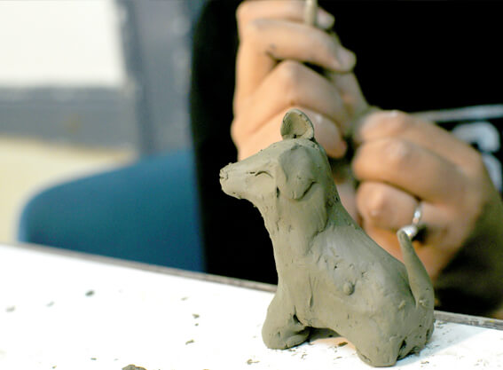 Person sculpting a small dog from clay