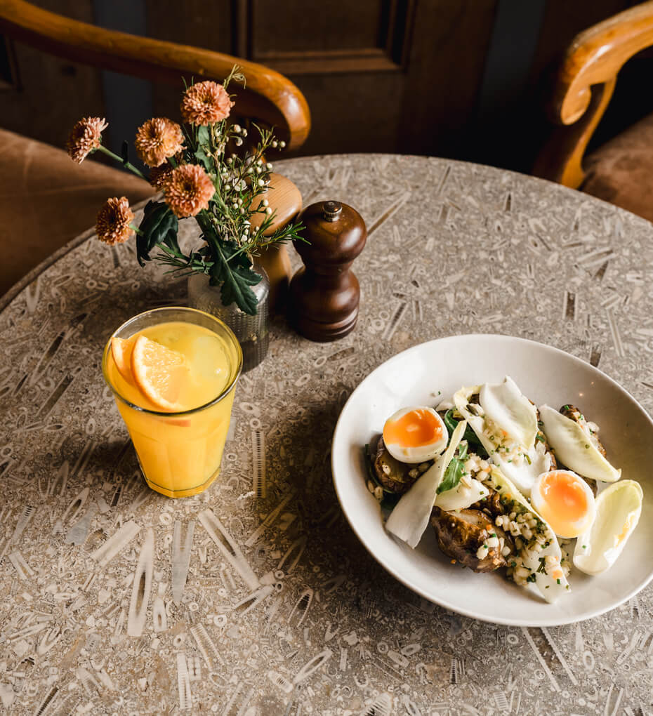 Cafe table with vase of flowers, glass of orange juice and an egg salad