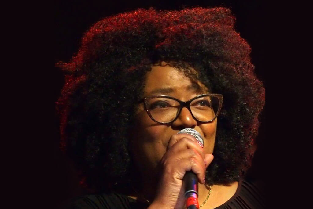 Woman of colour in glasses, singing into a microphone