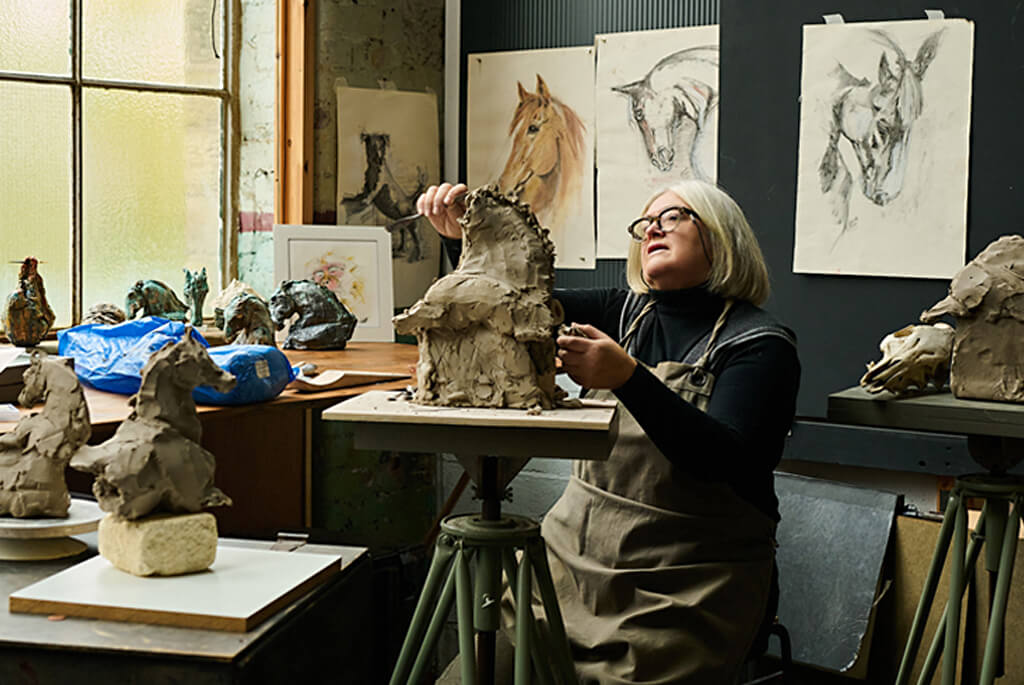 Woman sculpting horsehead in clay in her studio