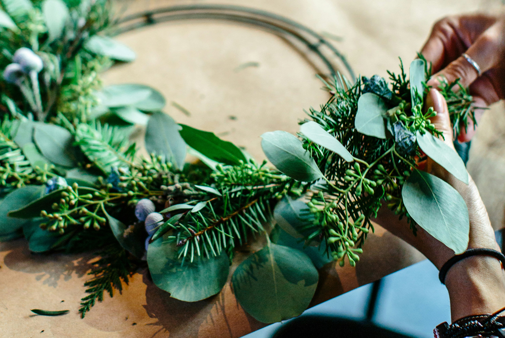 Hands shown holding and making a wreath made of natural foliage