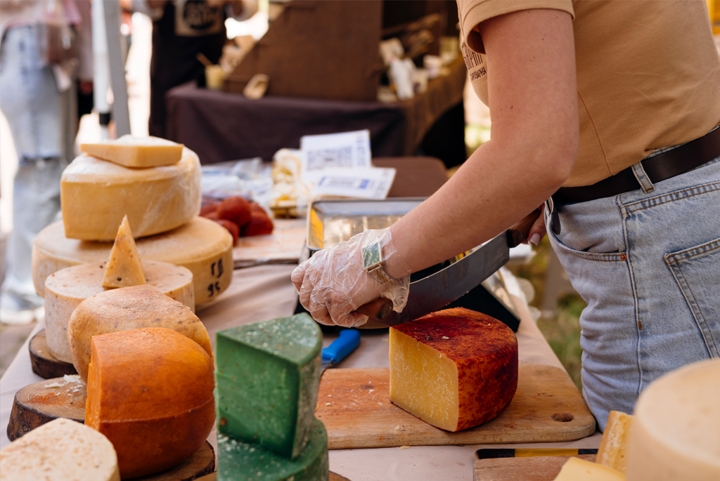 Woman cutting cheese from a selection on a market stall